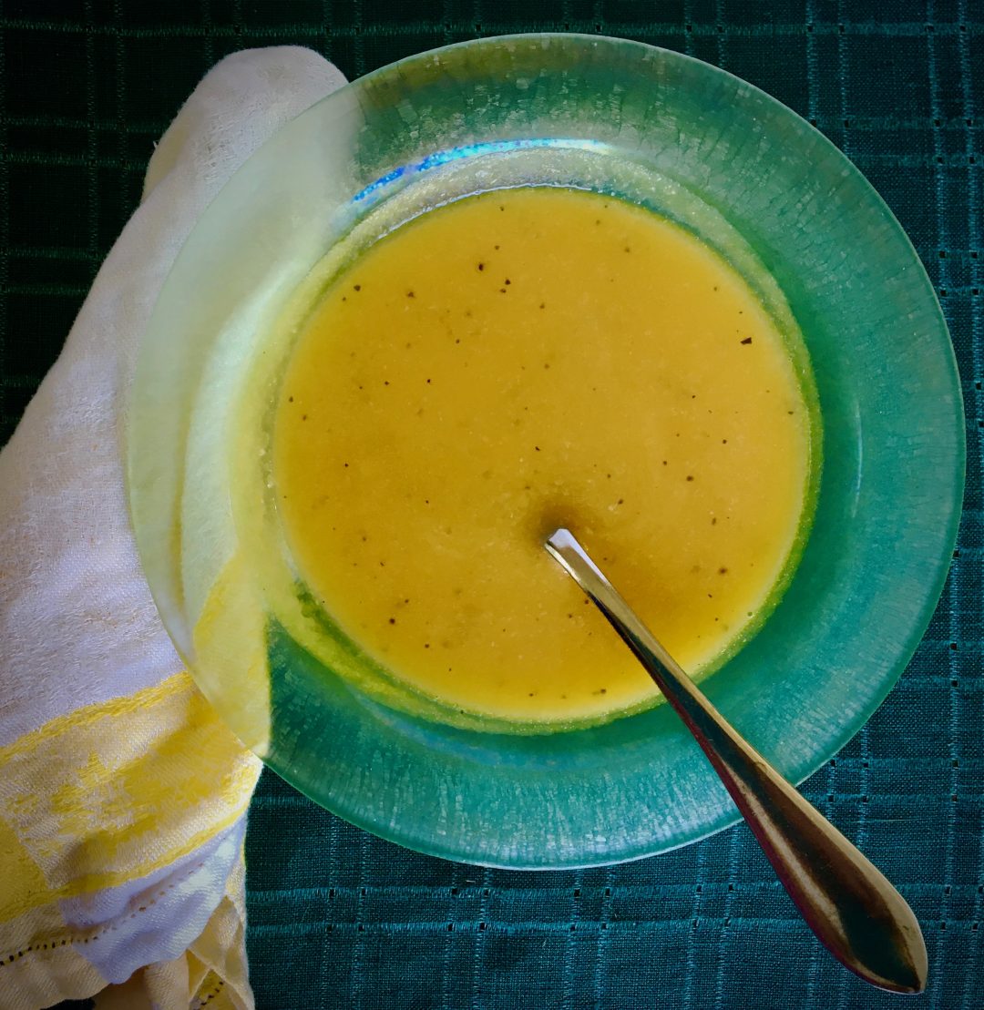 butternut squash soup in green glass soup dish with yellow and white napkin on green placemat with stainless steel spoon
