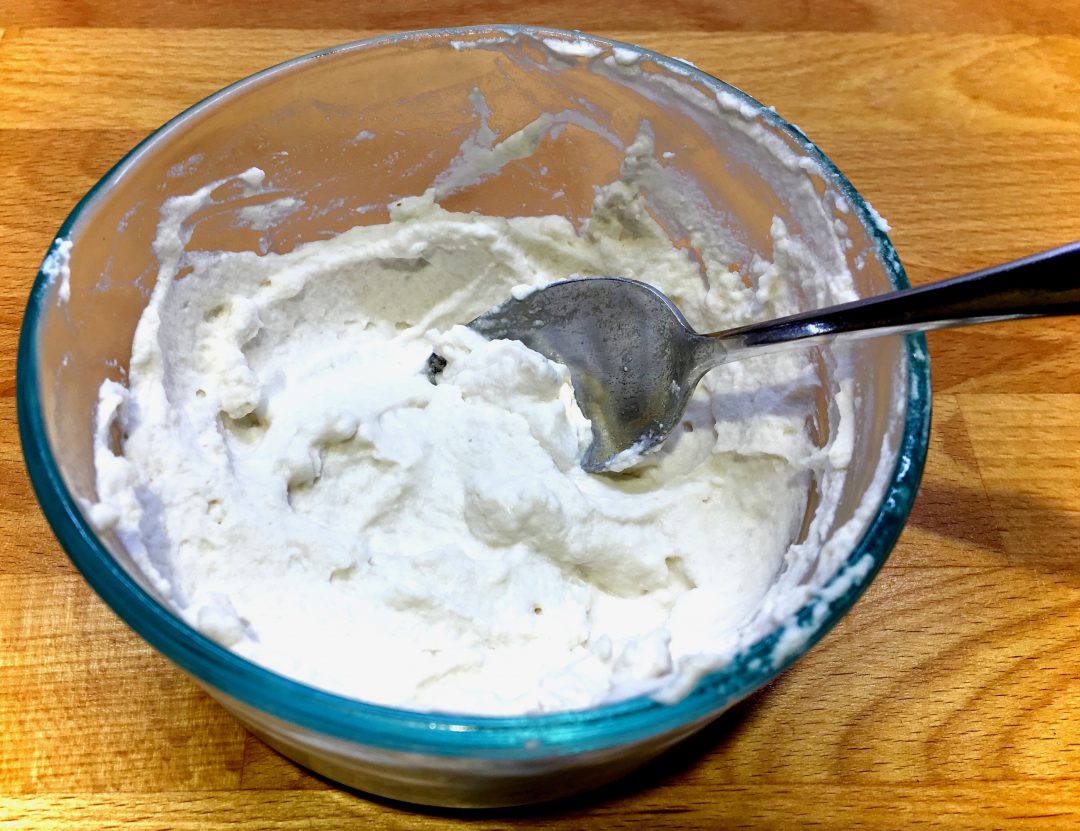 Coconut cream in a glass bowl with a stainless steel spoon in it on a wooden counter