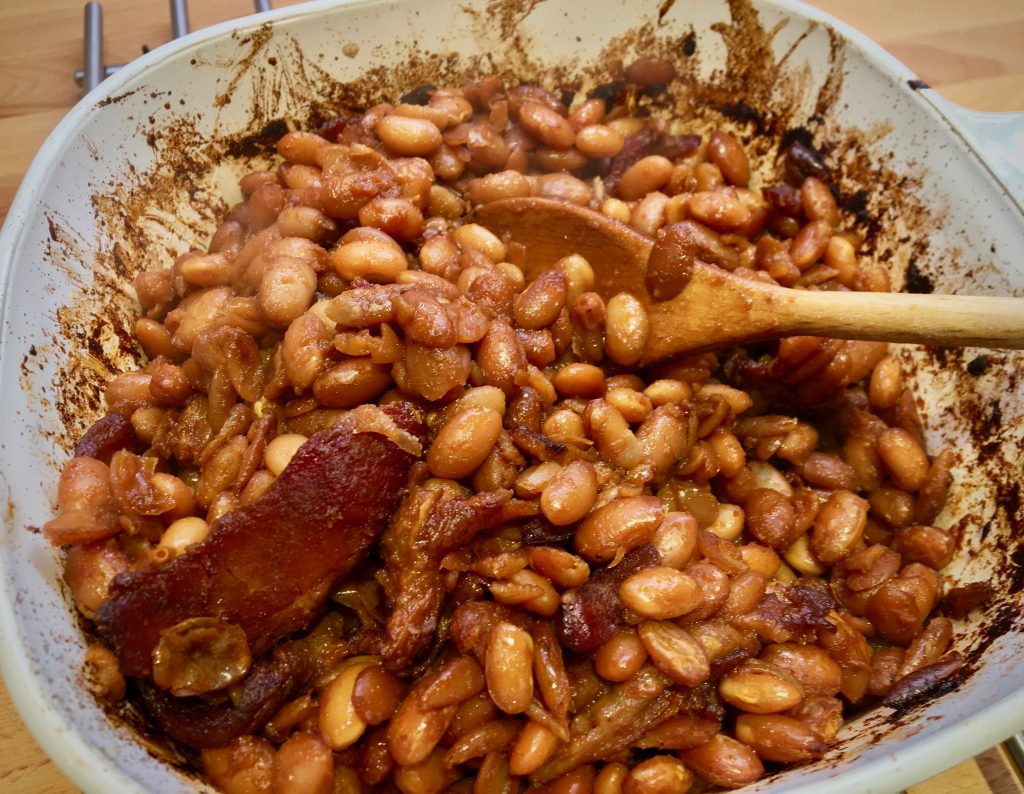 baked beans with bacon in a white ceramic baking dish with a wooden spoon