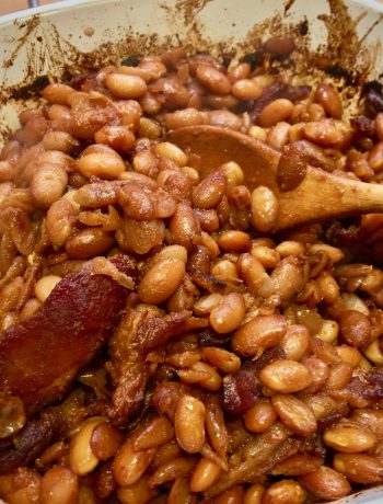 baked beans with bacon in a white ceramic baking dish with a wooden spoon