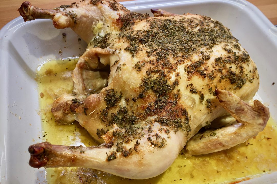 roast chicken with herb coating in white and red ceramic roasting pan