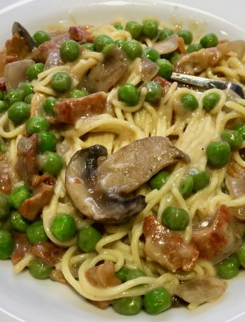 spaghetti with white sauce, peas, mushrooms and bacon on a white bowl with a fork