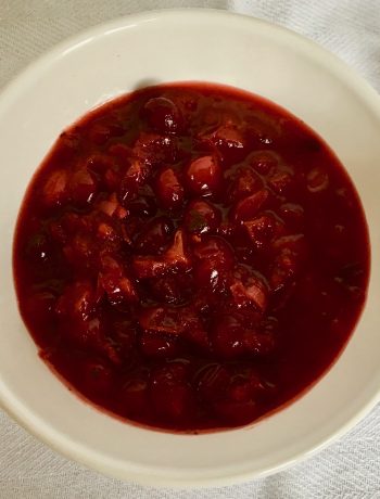 cranberry sauce in a white bowl on a white cloth with a silver spoon