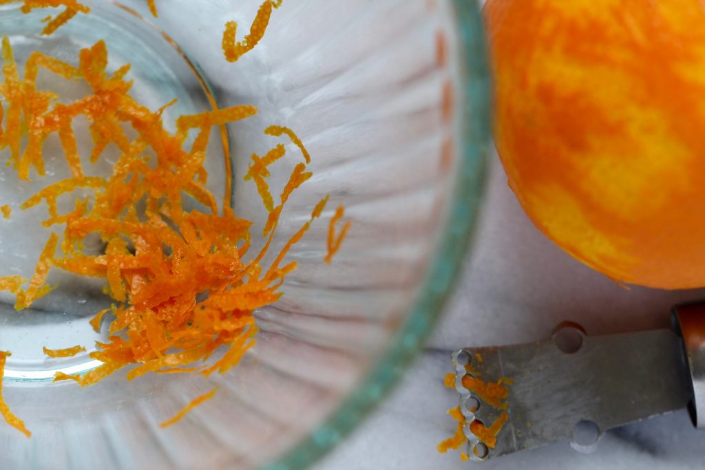 orange zest in a glass bowl next to a zested orange