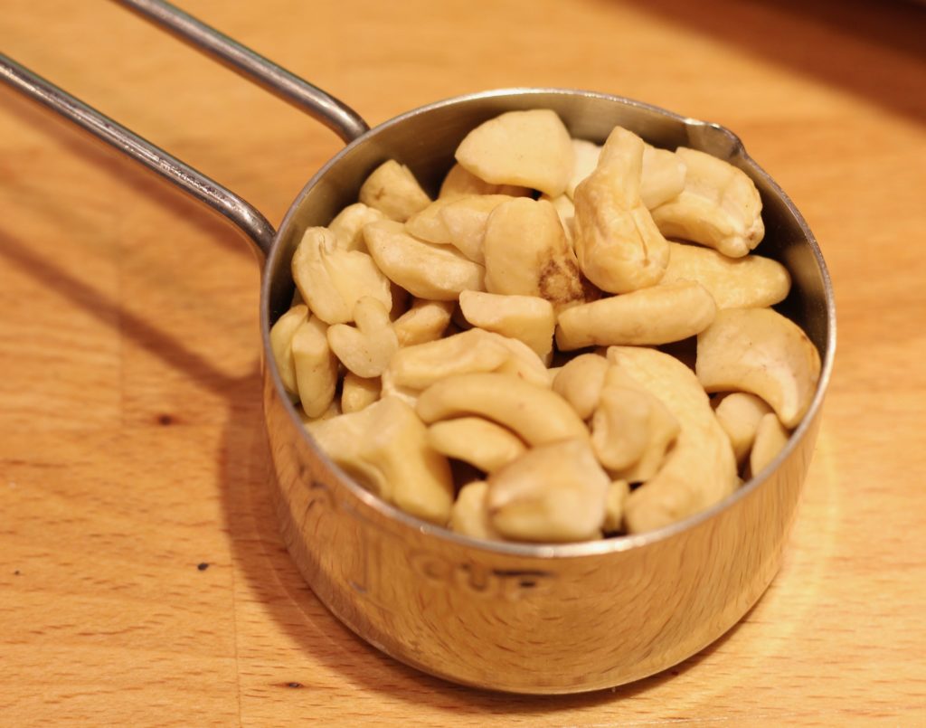 cashews in a stainless steel measuring cup on a wood counter