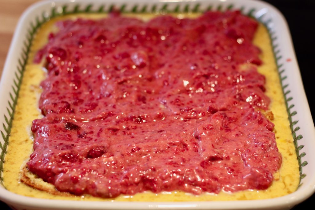 raspberry cream cheese mixture spread on top of toast in a ceramic baking dish