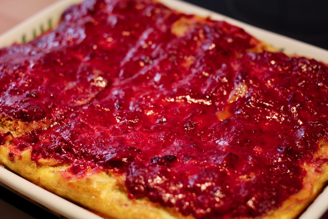 baked raspberry french toast in a ceramic baking dish on a black surface