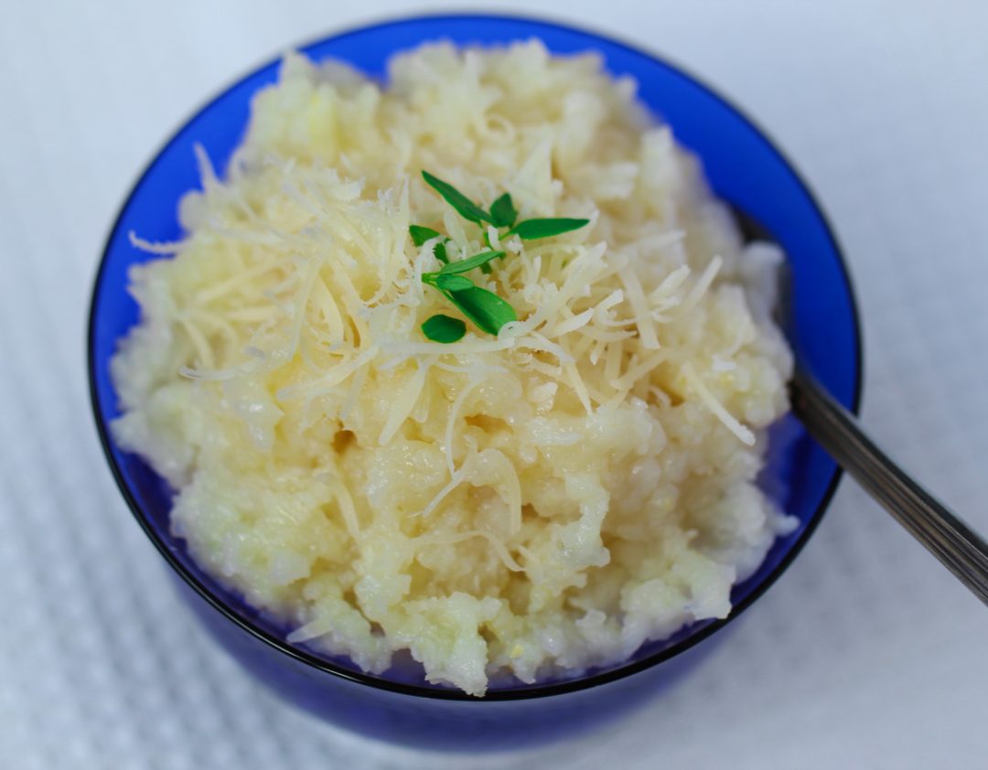 baked Arborio rice itopped with fresh thyme and grated non-dairy parmesan cheesen in a blue glass bowl on a white cloth