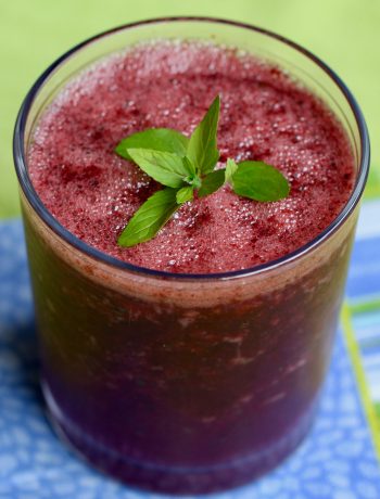 blueberry mint cooler in a glass with a sprig of mint on top on a blue napkin and green cloth
