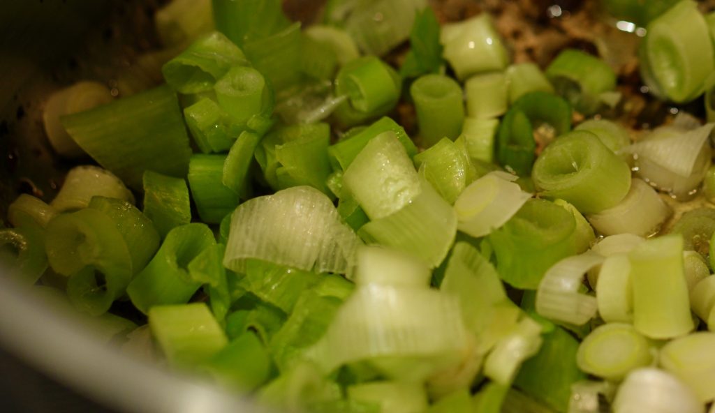 scallions cooking in oil in a stainless steel pan