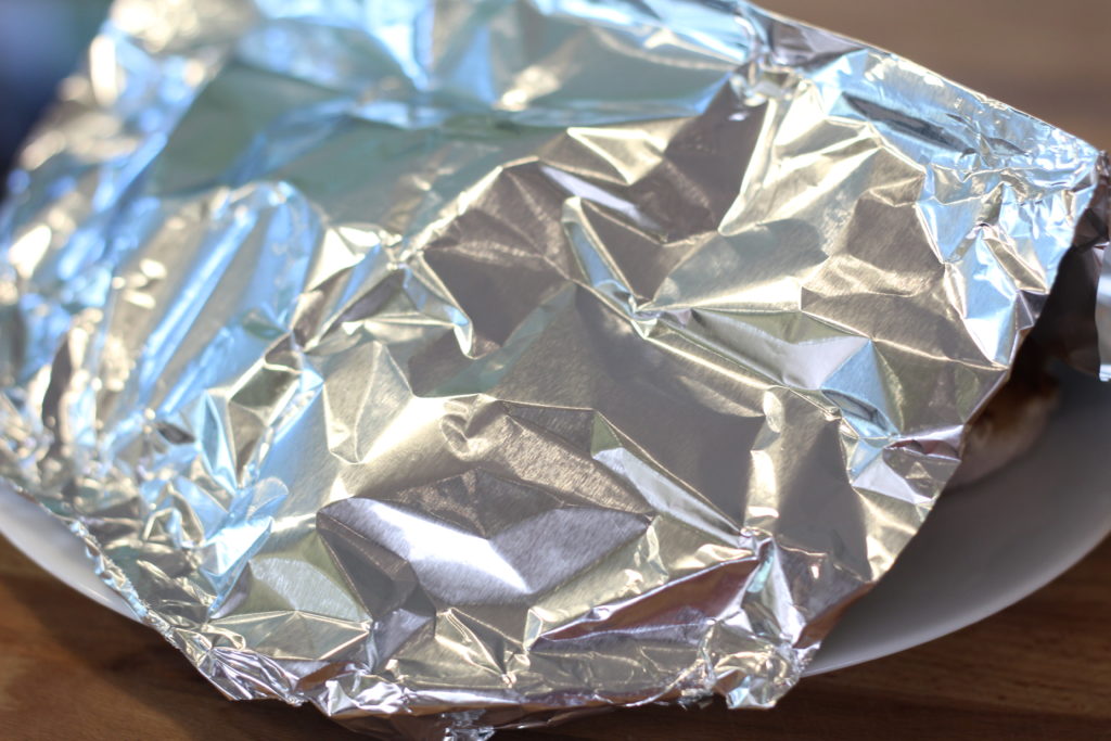 pork chops under a foil tent on a white ceramic plate