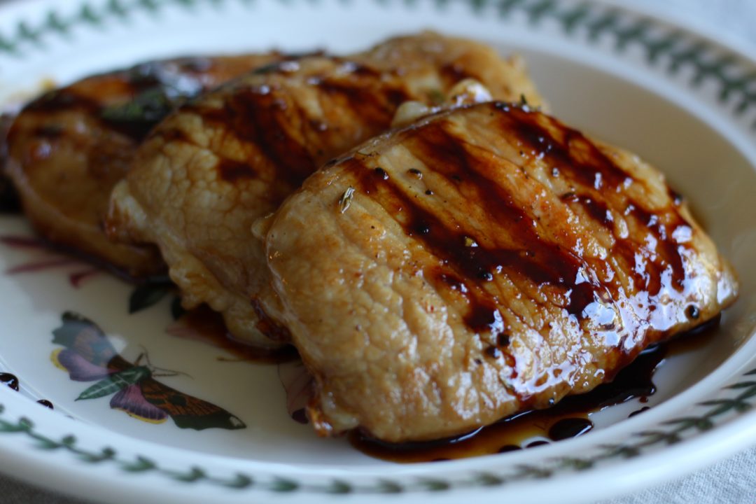 cooked pork chops on a white floral plate topped with apple cider vinegar glaze