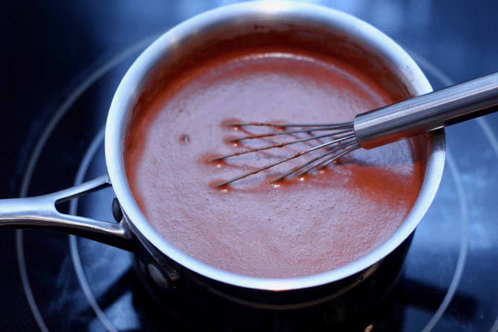 whisking dairy-free chocolate pudding in a stainless steel pan with a whisk