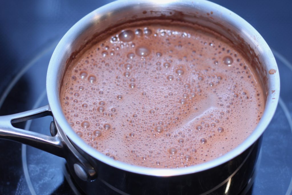dairy-free chocolate pudding coming to a boil in a stainless steel pan on a glass cooktop