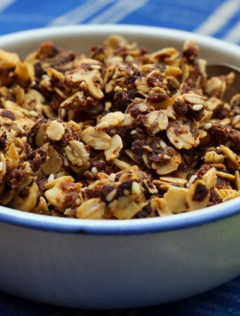 hazelnut granola in a white ceramic dish with a silver spoon on a blue and white cloth