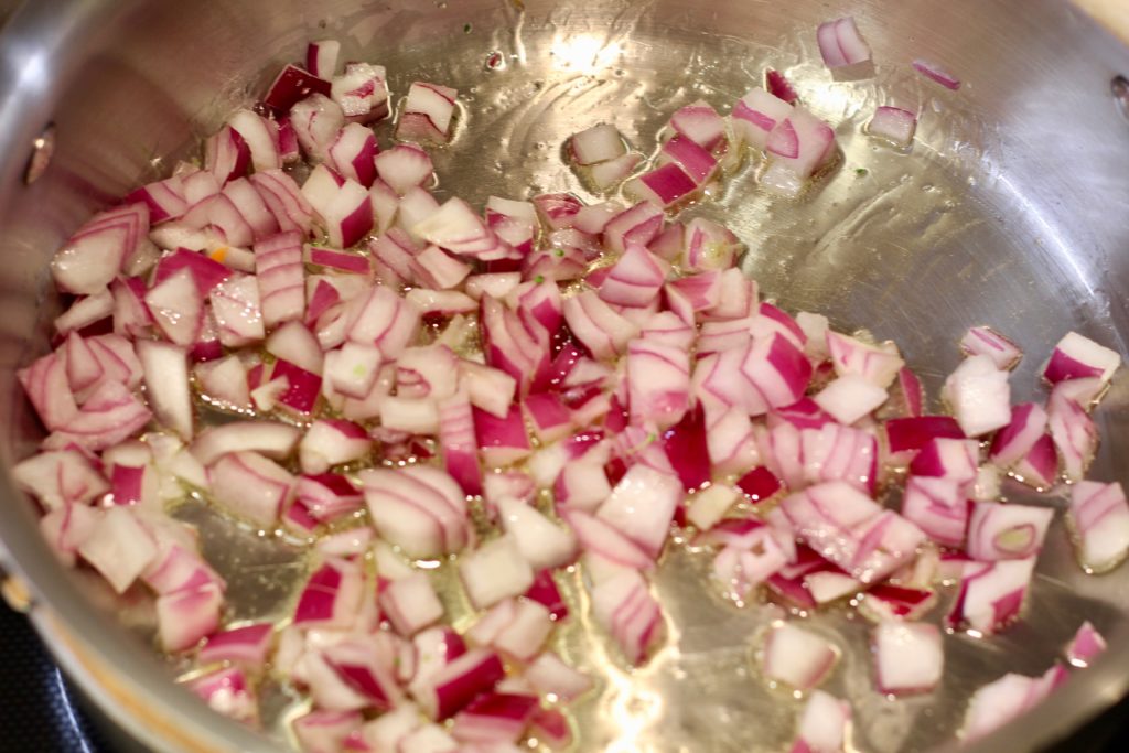 red onions cooking in a stainless steel pan