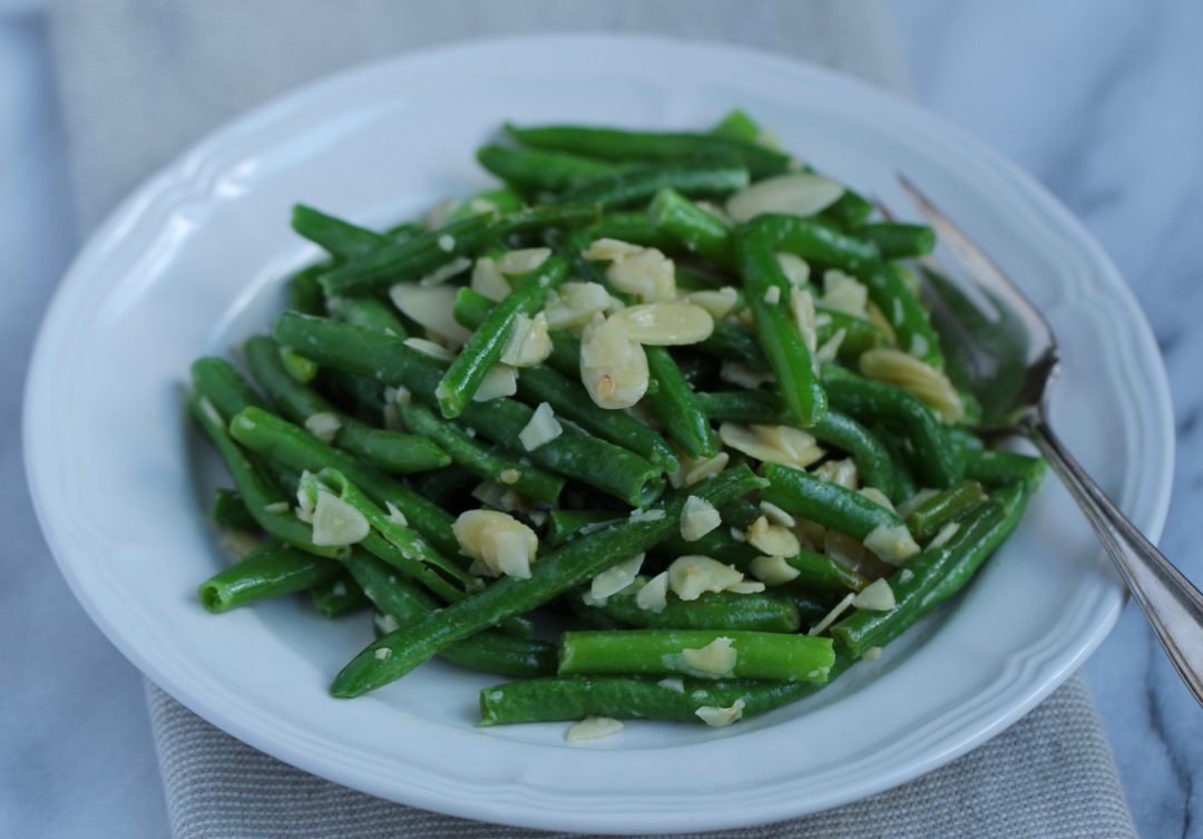 green beans with garlic and almonds on a white plate