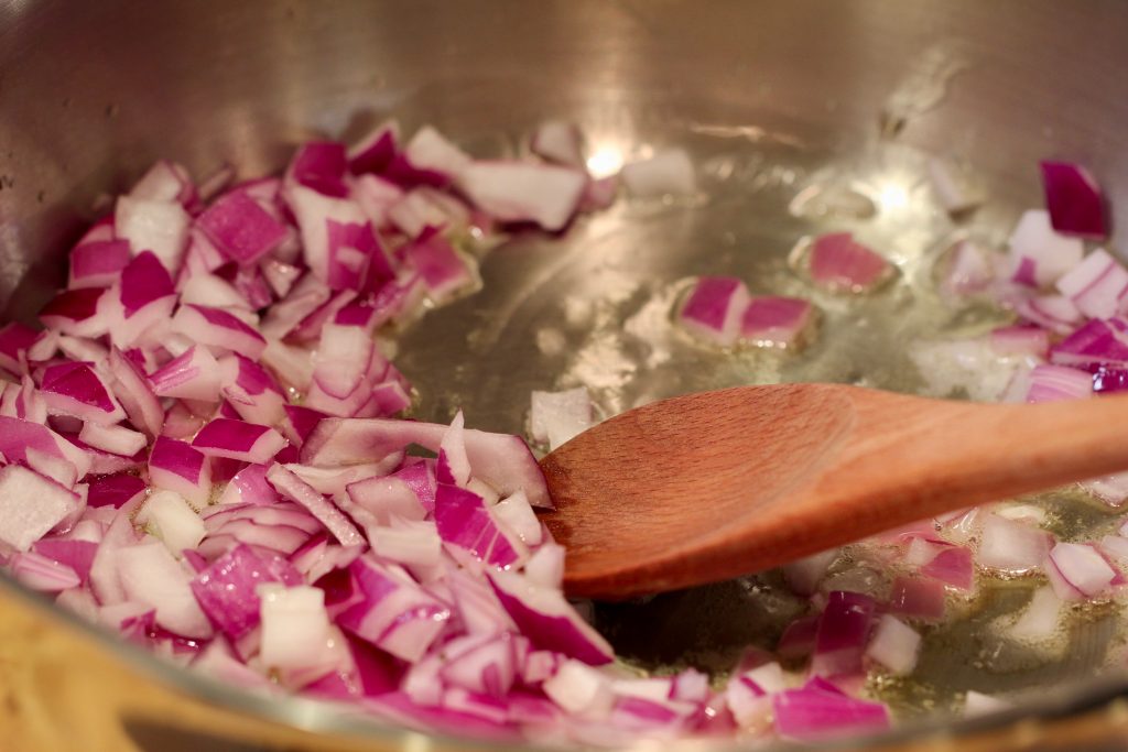 red onions sautéd in stainless steel pan with wooden spoon