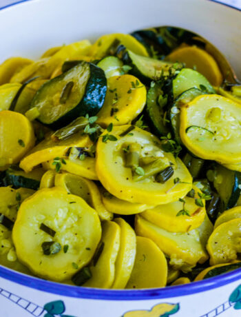 Green and yellow summer squash with garlic scapes in a white bowl