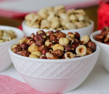 bowls of hazelnuts, cashews in white bowls on a red and white cloth